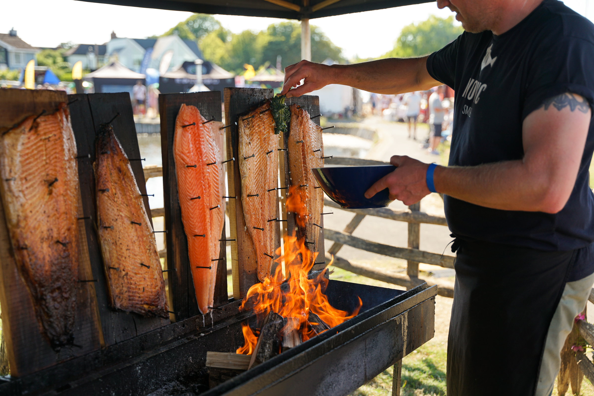 A person cooking fish over an open fire at a festival.